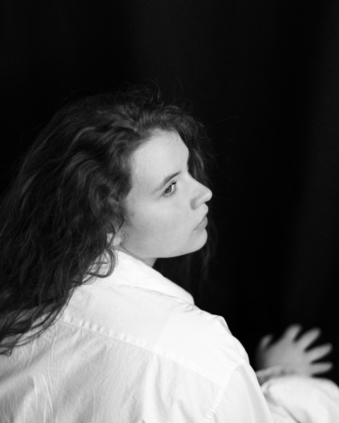 Black and white portrait of a woman in a white shirt, looking over her shoulder.