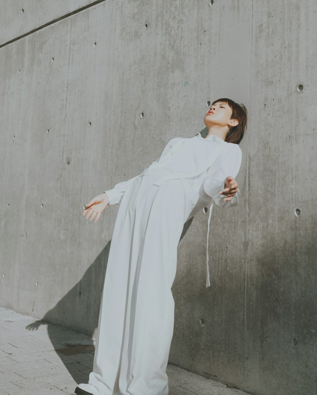 A model in a loose pale linen outfit against a concrete wall