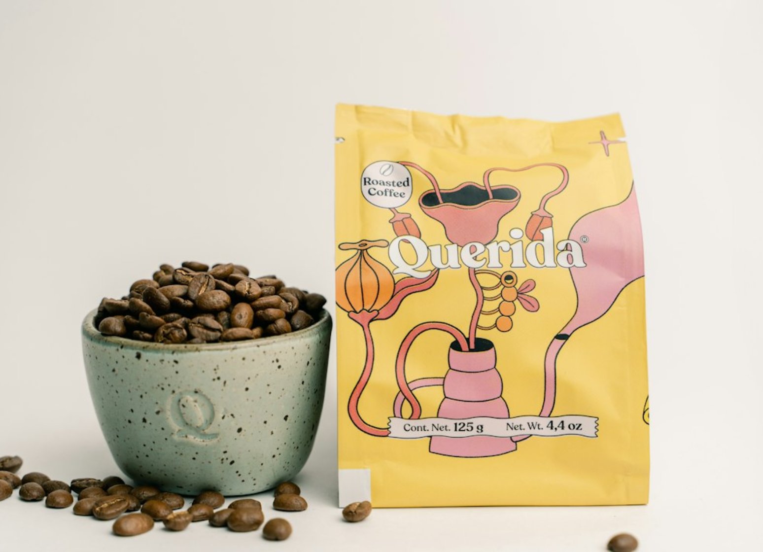 A bag of Ferro coffee beside a ceramic cup heaped with roasted beans